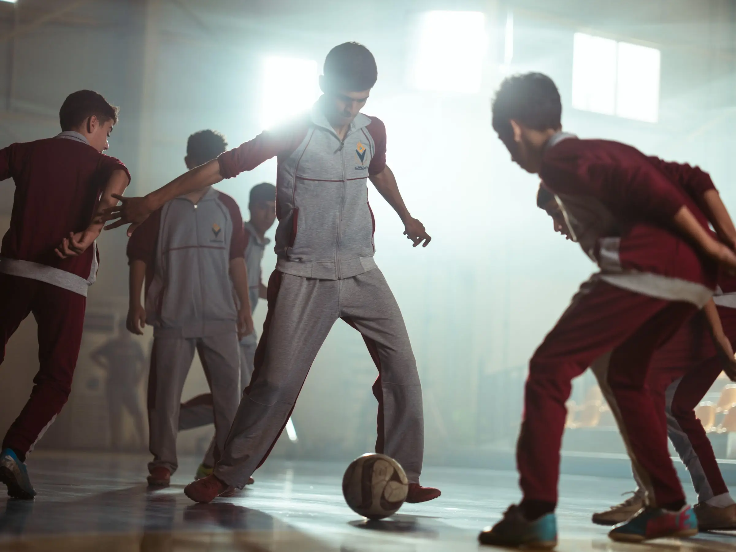 Young players contesting the ball on a polished indoor court under dramatic evening light